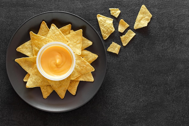 Nachos an appetizer of Mexican cuisine with cheese salsa on plate on dark background top view space to copy textxA