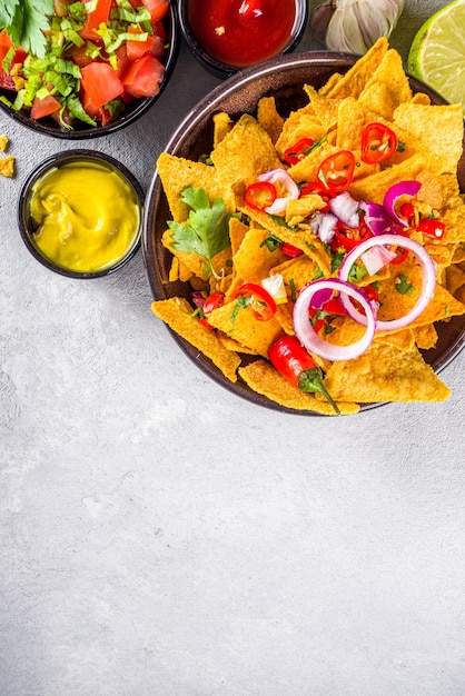 Nachos-chips met gesmolten kaas en verschillende traditionele mexicaanse dips, salsa en jalapeno, donkergrijze achtergrond bovenaanzicht kopieerruimte