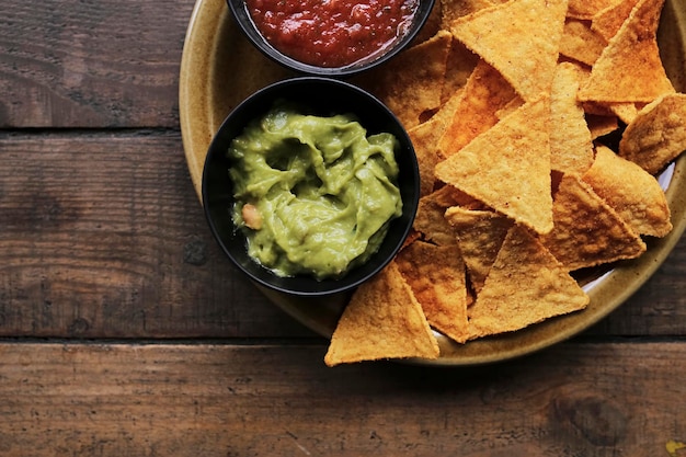 Nachos chips met salsa en guacamole saus op een bruin bord op een houten ondergrond, bovenaanzicht.