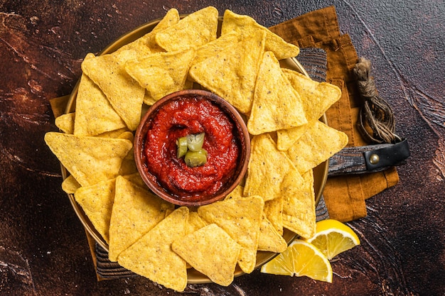 Nachos chips with tomato sauce and jalapeno mexican appetizer Dark background Top view