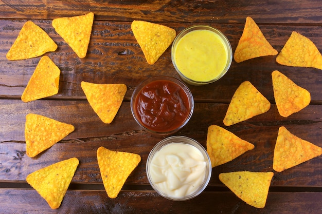 Nachos corn chips spread on wooden table next to assorted sauces