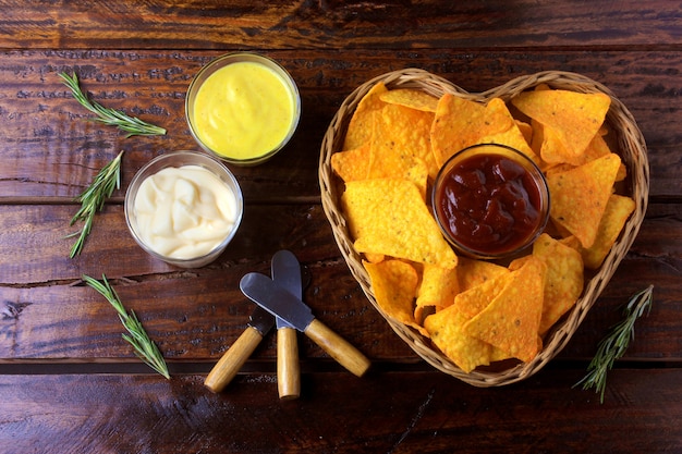 Nachos corn chips with sauces placed in basket with heart shape on wooden table