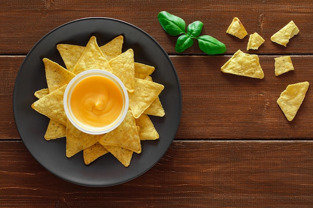 Nachos whole and broken with cheese salsa leaf of green basil on plate on wooden brown plank tabletop background top view space to copy textxD