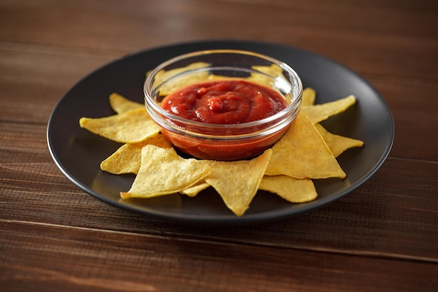 Photo nachos with tomato salsa on gray plate on brown wooden table top selective focus