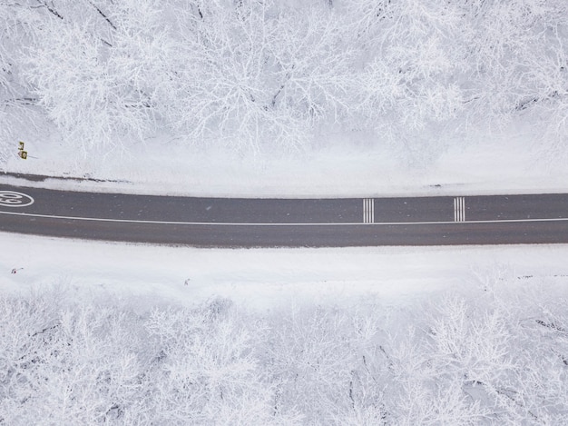 Nachtelijke luchtfoto van boven naar beneden van een besneeuwde weg omringd door dennenbos in het winterseizoen.