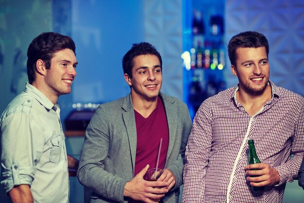 nachtleven, feest, vriendschap, vrije tijd en mensen concept - groep lachende mannelijke vrienden met bierflesjes drinken in nachtclub