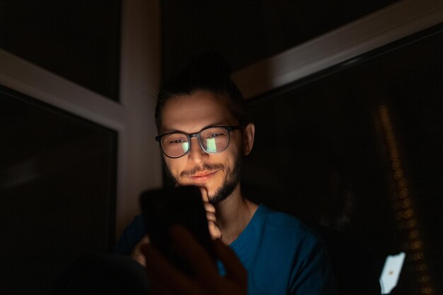 Nachtportret van jonge lachende man met smartphone in de hand