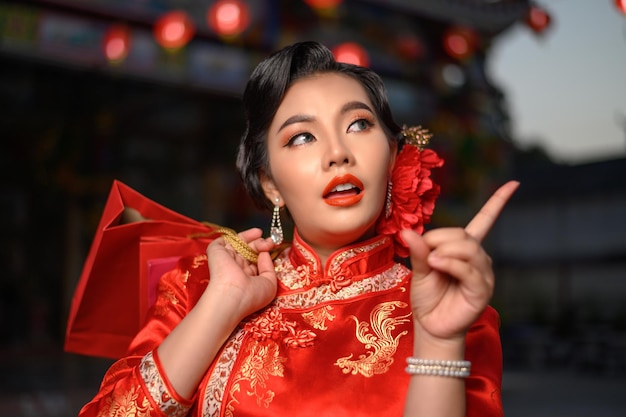 Nachtscène, Portret Aziatische mooie vrouw die een cheongsam draagt die lacht en poseert met boodschappentassen bij heiligdom op Chinees Nieuwjaar