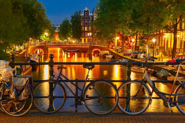 Nachtverlichting van het kanaal en de brug van Amsterdam met typisch Nederlandse huizen, boten en fietsen, Holland, Nederland.