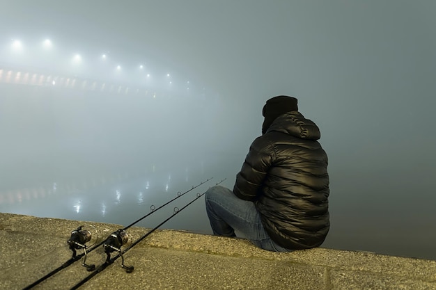 Foto nachtvissen urban edition. visser in mistige nacht. nachtvissen, karperhengels, nachtreflectie. stadslichten.