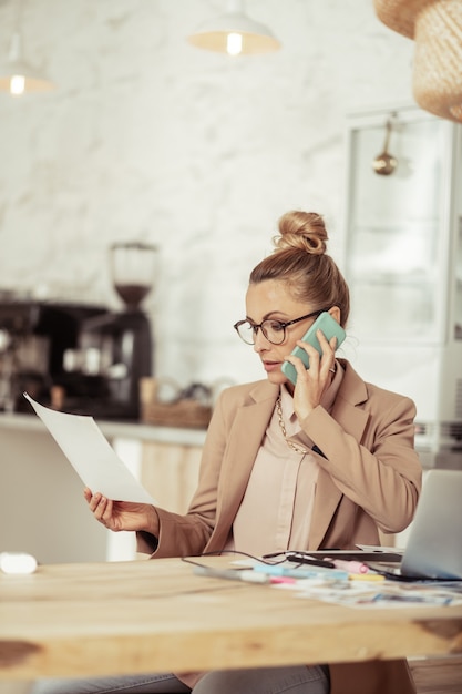 Nadenken over details. Geconcentreerde modestyliste die haar schetsen vasthoudt en aan de telefoon met de klant praat.