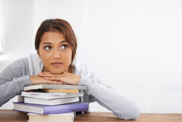 Nadenken over oplossingen voor een probleem Close-up shot van een aantrekkelijke studente die op haar boeken leunt en er bedachtzaam uitziet