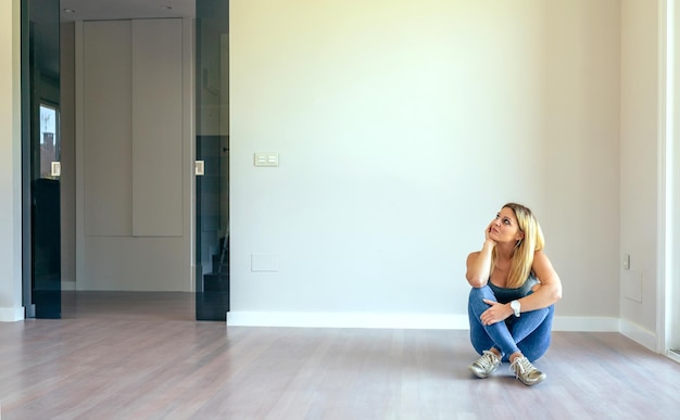 Nadenkend blond meisje zit in een lege woonkamer