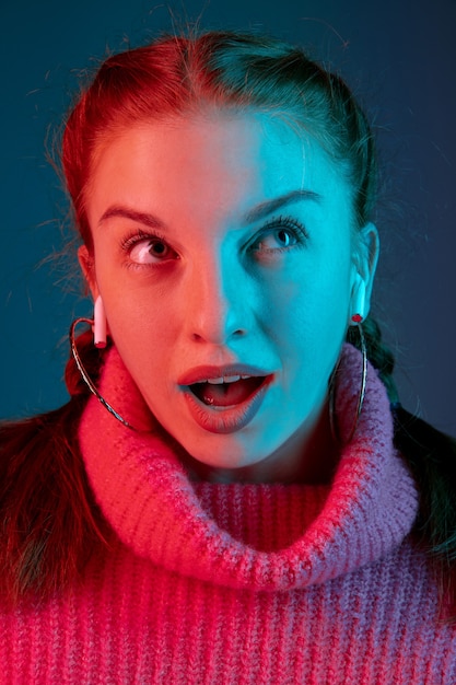 Nadenkend, close-up. Het portret van de blanke vrouw geïsoleerd op de achtergrond van de gradiëntstudio in neonlicht. Mooi vrouwelijk model met rood haar. Concept van menselijke emoties, gezichtsuitdrukking, verkoop, advertentie.