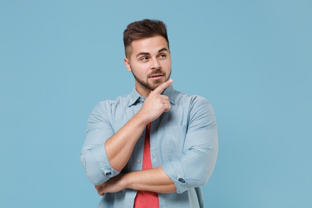 Nadenkend jonge bebaarde man 20s in casual shirt poseren geïsoleerd op pastel blauwe achtergrond studio portret. Mensen emoties levensstijl concept. Bespotten kopie ruimte. Zet de handsteun op de kin en kijk opzij.
