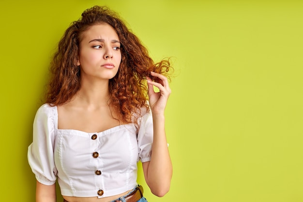 Nadenkend krullend meisje kijkt naar gespleten haarpunten, onderzoekt het, wil eruit knippen