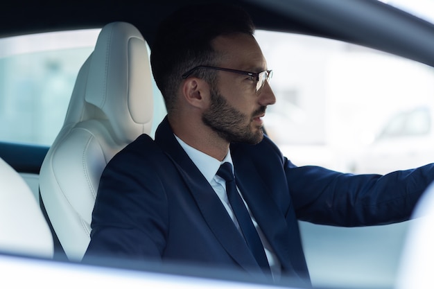 Nadenkend mens. Welvarende, bebaarde jonge zakenman die zich attent voelt tijdens het autorijden