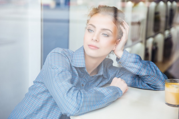 Nadenkend mooie jonge vrouw in blauw shirt zitten en denken in café