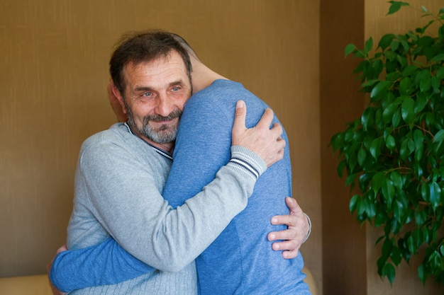 Nadenkend senior man knuffelen zijn volwassen zoon