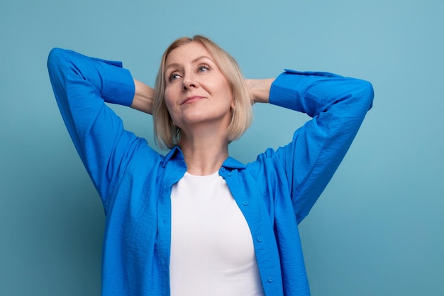 Nadenkend volwassen vrouw met blond haar dromen op blauwe achtergrond met kopie ruimte