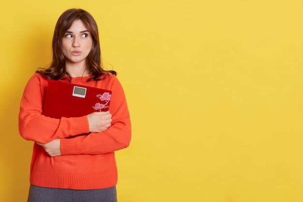 Nadenkend vrouw wegkijken met pruillip lippen, vloerweegschalen omhelst, denkt aan dieet en afvallen