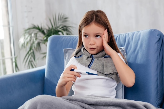 Nadenkend ziek meisje kijkt weg terwijl ze de thermometer in de hand houdt