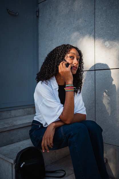 Nadenkende Afrikaanse vrouw die telefoneert terwijl ze op een trap zit