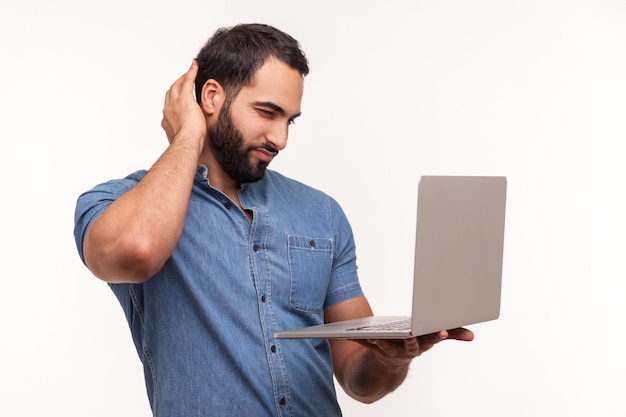 Nadenkende bebaarde man kijken naar laptop scherm wrijven zijn achterkant van hoofd niet begrijpen besturingssysteem cant applicatie Indoor studio shot geïsoleerd op witte achtergrond installeren