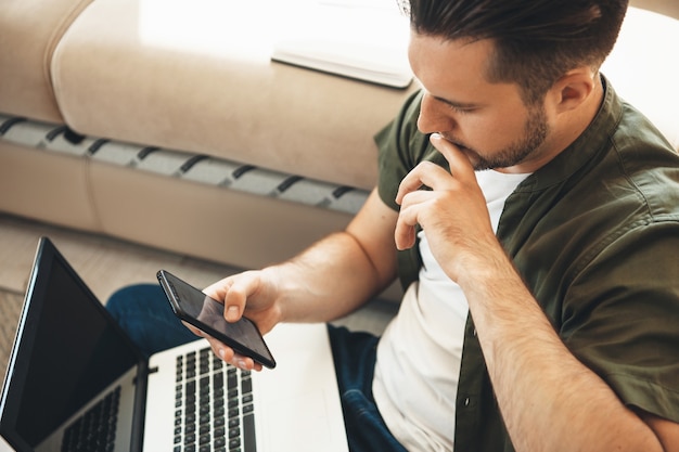 Nadenkende blanke man met baard werkt vanuit huis op de computer tijdens het chatten op mobiel