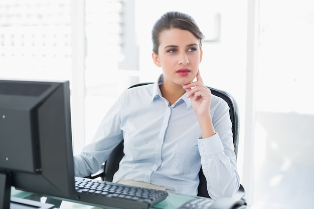 Nadenkende elegante bruine haired onderneemster die een computer met behulp van