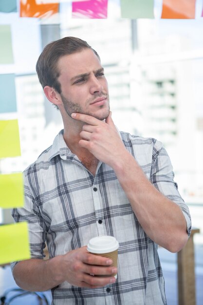 Nadenkende hipstermens met koffie in bureau