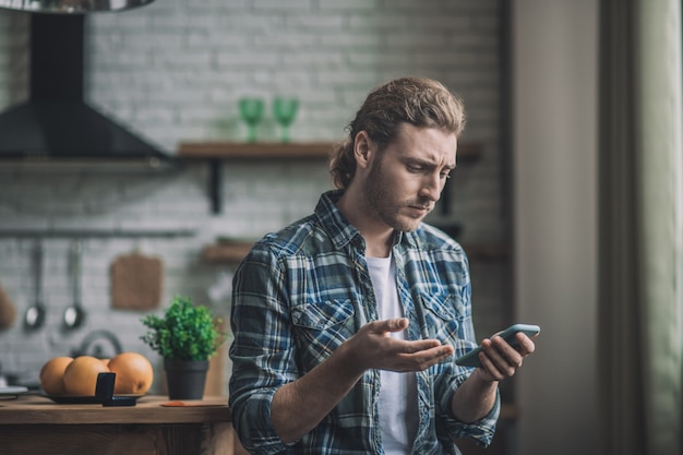 Nadenkende jonge man met zijn smartphone thuis