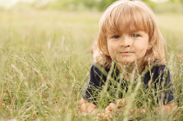 nadenkende kleine jongen krullend blond liggend op een groen gazon zomer natuur