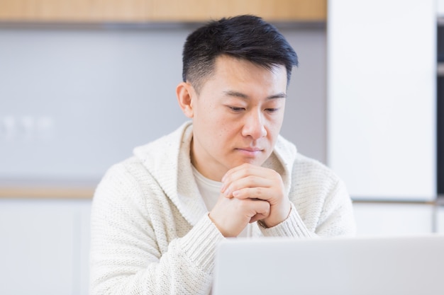 Nadenkende serieuze jonge aziatische man die wegkijkt student schrijver zit thuis bureau met laptop