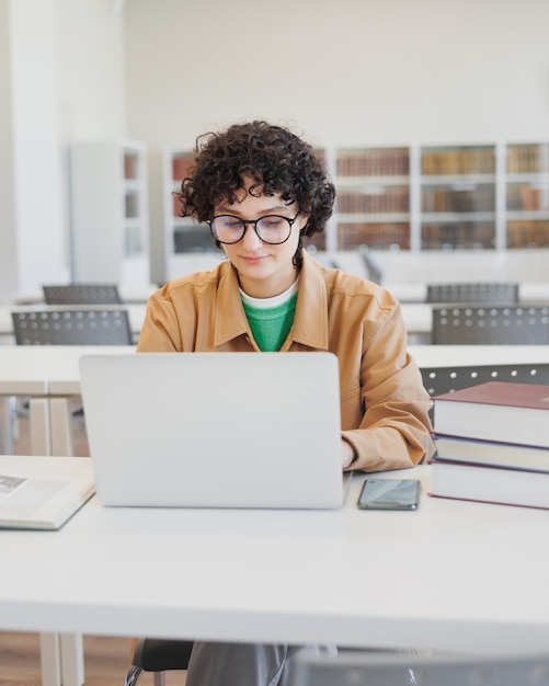 Nadenkende vrouw werkt in bibliotheek, kijkt naar een educatief webinar op internet, verveelt zich met coworking achter laptop
