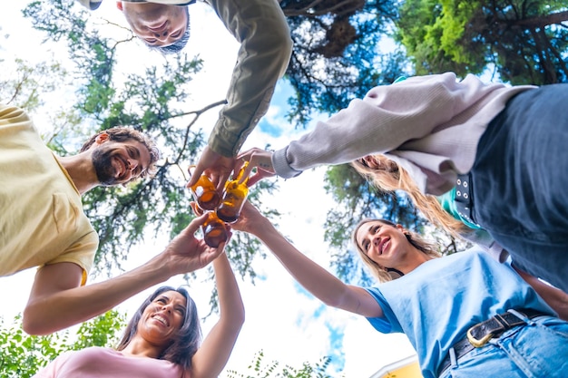 Nadir shot van een groep multi-etnische vrienden die in het stadspark zitten te proosten met flesjes bier