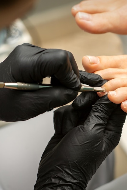 Nagelriemverwijdering op tenen. Handen in zwarte handschoenen van pedicure meester verwijderen cuticula op vrouwelijke tenen door pusher.