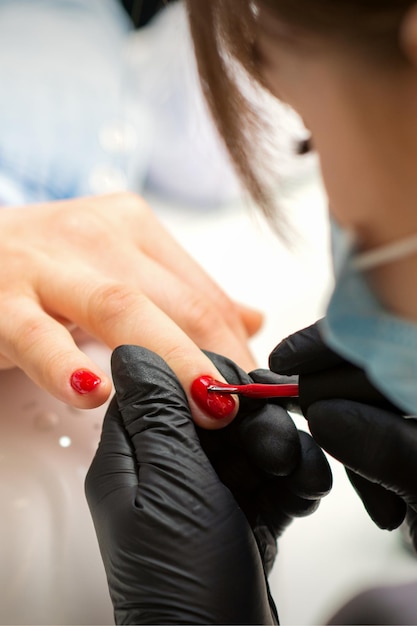 Nagels lakken van een vrouw. Handen van manicure in zwarte handschoenen rode nagellak toe te passen op vrouwelijke nagels in een schoonheidssalon.