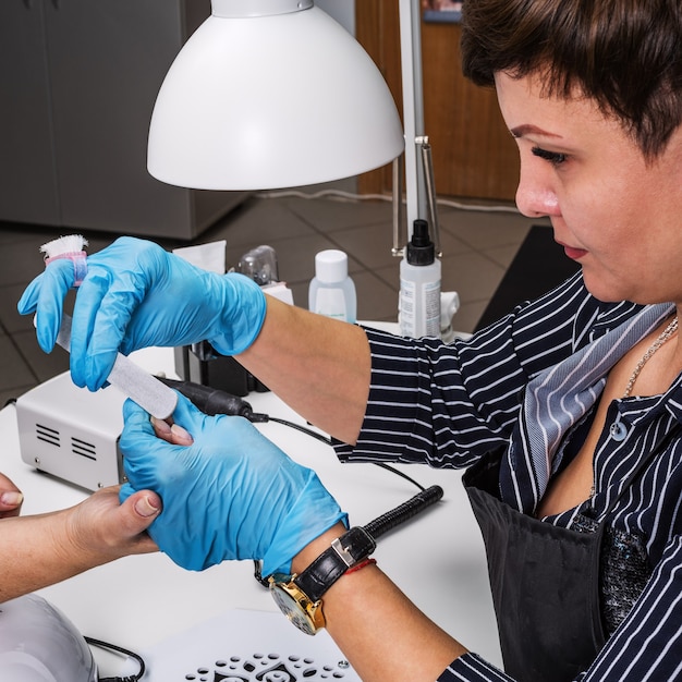 Nagelsalon, handen van cliënt en meester close-up. Nagelbehandeling met een manicurevijl