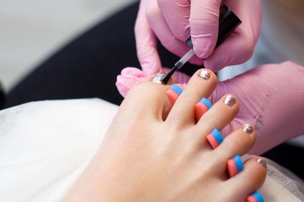 Nagelverzorging en pedicure concept. De close-upmanicure dient roze handschoenen in is het schilderen van gouden Nagellak op de tenen van de Cliënt.
