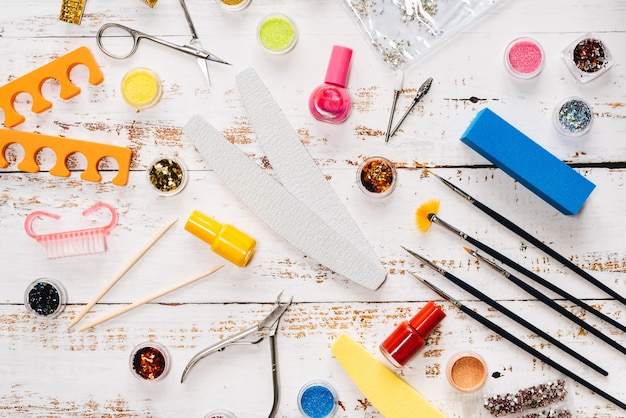 Nagelvijlen, schaar, tang, pailletten en nagellakken op een witte houten tafel.