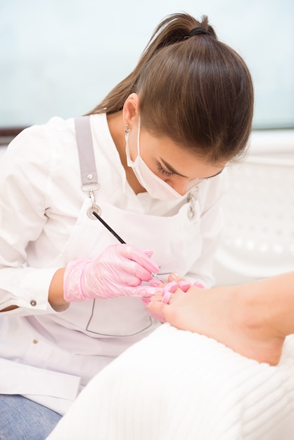 Nail artist in beauty salon making pedicure for clients feet.