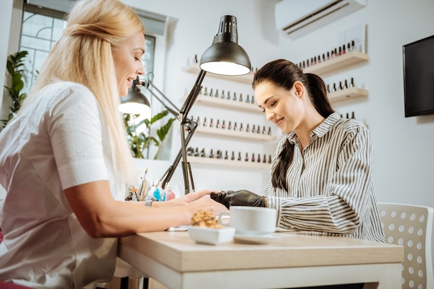 nail artist. pleasant dark-haired nail artist feeling good talking to her constant client while working