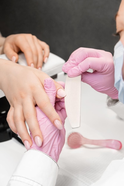 nail beautitian using a nail file to correct the form of a gel base polish close up