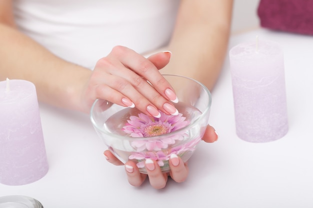 Nail Care. Closeup Of Beautiful Woman Hands With Natural Nails In Beauty Salon. Female Soaking Fingernails In Transparent Glass Bowl Full Of Water Indoors. Spa Manicure Concept. High Resolution