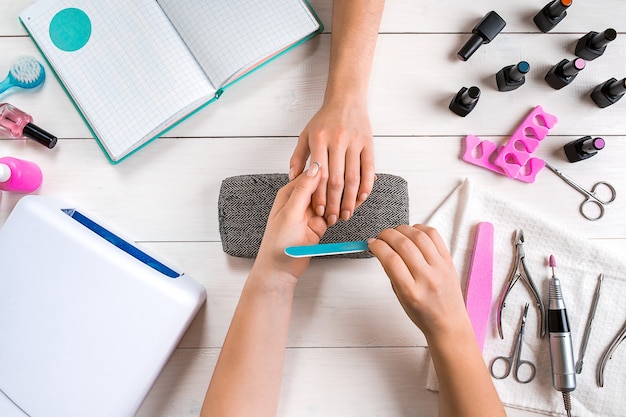 Nail care closeup of female hands filing nails with professional nail file in beauty nail salon top ...