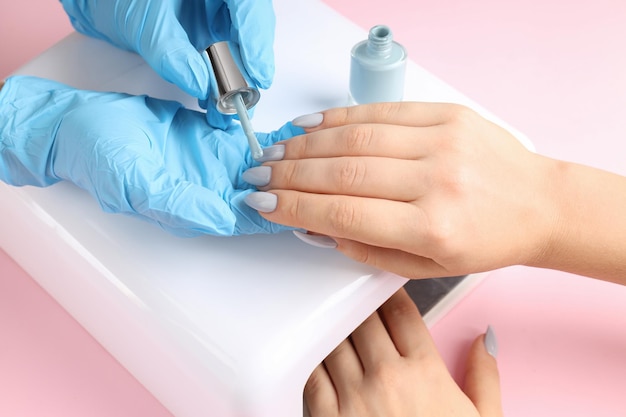 Nail care procedure on pink background, close up