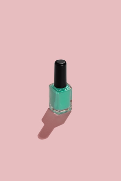 A nail enamel bottle on pink background with hard sunlight shadow