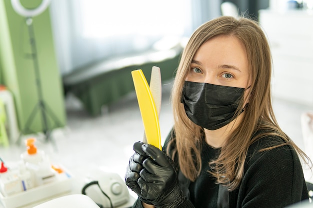 Nail file in the manicurist's hand. Attractive young woman is spending time in beauty salon while doing manicure.