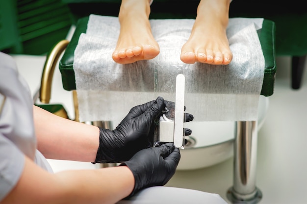 Nail file tool in hands of chiropodist before procedure files nails on toes in a nail salon